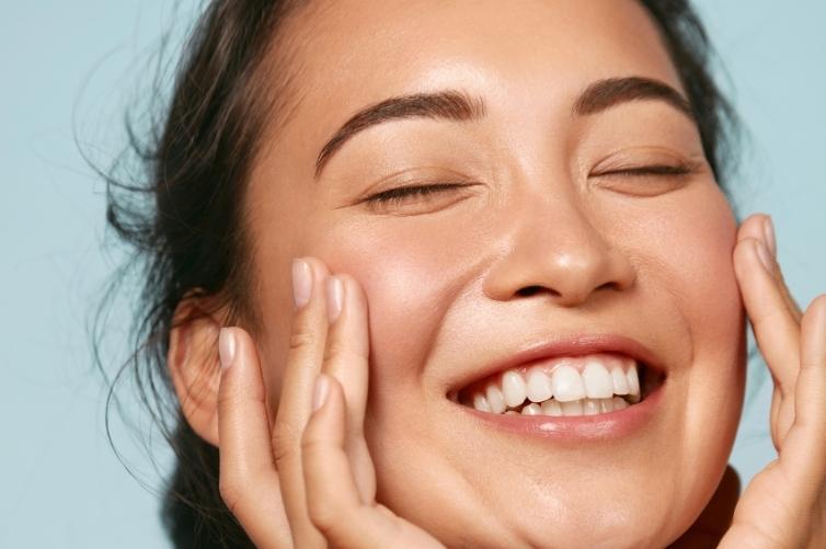 Mutlu genç kadın yüzüne dokunarak gülümsüyor, mavi arka plan